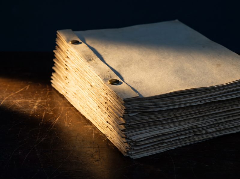 A tall stack of loose brass-bound paper on a dark table